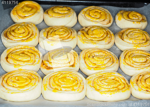 Image of Closeup of raw cinnamon buns after proofing with egg yolk, on ba