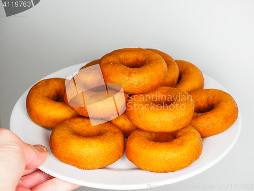 Image of Male person holding a plate of freshly made dark brown doughnuts