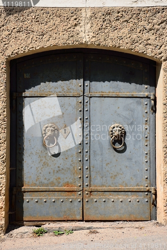 Image of Old iron door with lion handles on a stone wall