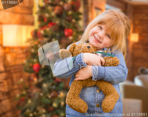 Image of Girl Holding Teddy Bear In Front of Decorated Christmas Tree