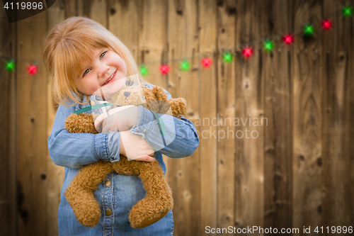Image of Girl Holding Teddy Bear In Front of Wooded Background with Chris