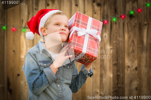 Image of Curious Boy Wearing Santa Hat Holding Christmas Gift On Wood