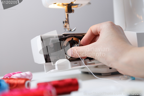 Image of Woman inserts bobbin in sewing-machine