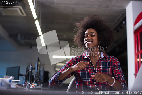 Image of black woman in modern office speeking on phone over earphones