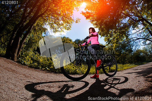 Image of Young woman having fun riding a bicycle in the park.