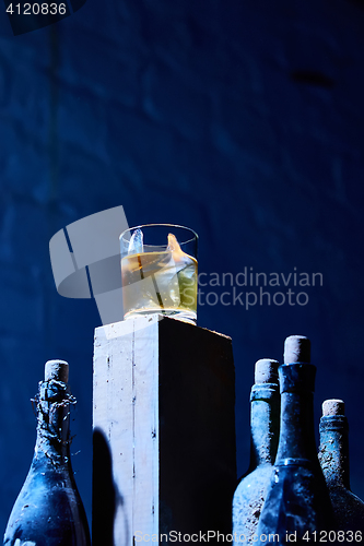 Image of Glass of whiskey with ice on old wooden bar around the  bottles