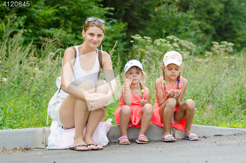 Image of Mother and two children sitting on the curb of the road waiting for the bus