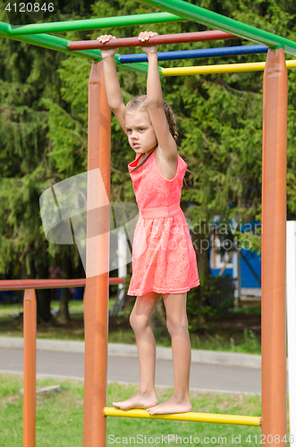 Image of The girl in the pink dress on the horizontal bar climbing on playground