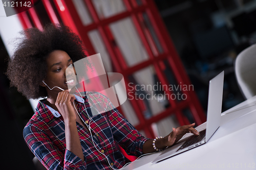 Image of black woman in modern office speeking on phone over earphones