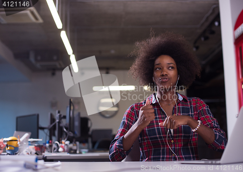 Image of black woman in modern office speeking on phone over earphones