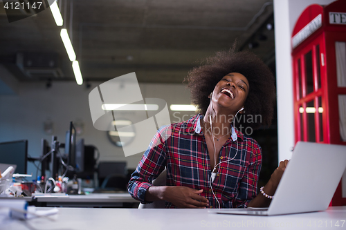 Image of black woman in modern office speeking on phone over earphones