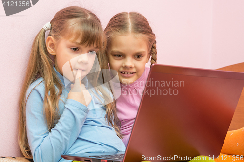 Image of Funny girl put a finger in his mouth sitting at a laptop