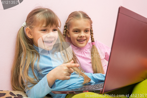 Image of Two girls looking at a laptop and laughing merrily, one is pointing at the screen