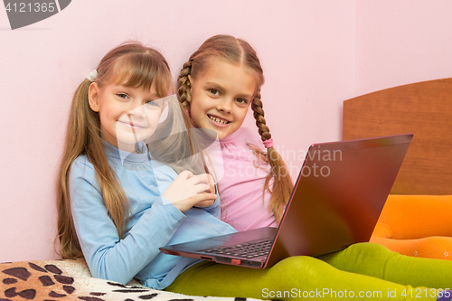 Image of Two girls sitting on a bed with a laptop and a fun look into the frame