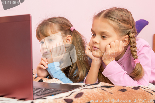 Image of Two girls lying on his stomach on the bed looking at the laptop screen