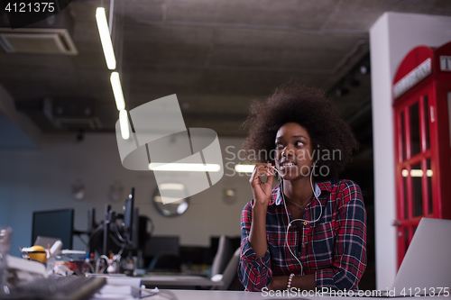 Image of black woman in modern office speeking on phone over earphones