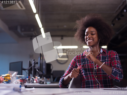 Image of black woman in modern office speeking on phone over earphones