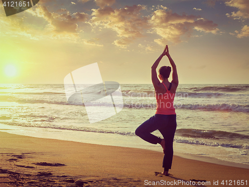 Image of Young sporty fit woman doing yoga tree asana on beach