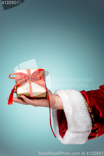Image of Hand of Santa Claus holding a gift on blue background