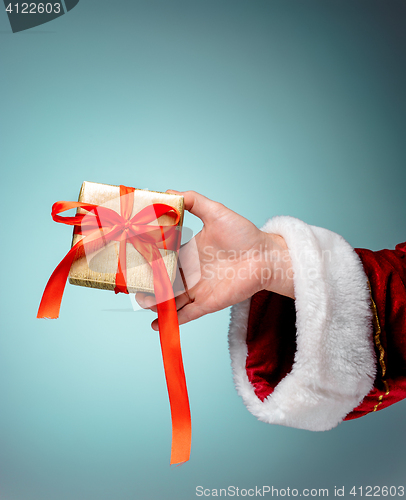 Image of Hand of Santa Claus holding a gift on blue background