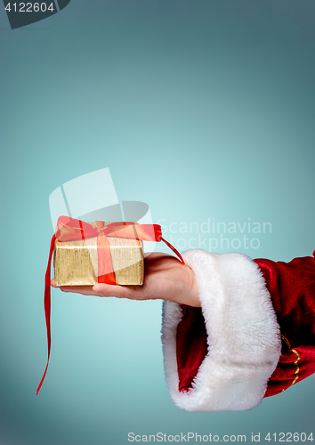 Image of Hand of Santa Claus holding a gift on blue background