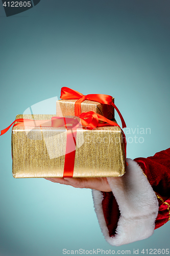 Image of Hand of Santa Claus holding a gift on blue background