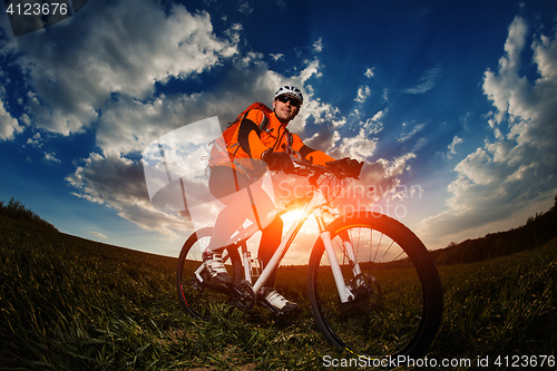 Image of biker in orange jersey riding on green summer field