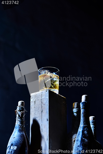 Image of Glass of whiskey with ice on old wooden bar around the  bottles