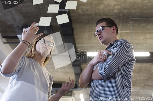 Image of young couple at modern office interior writing notes on stickers