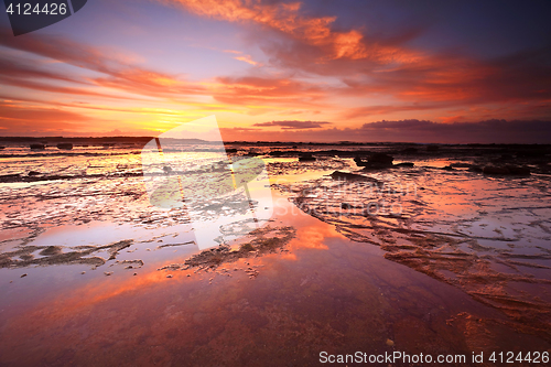 Image of Sunrise skies reflecting on the exposed rocks in low tide