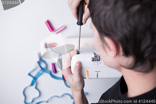 Image of Man with screwdriver repairing sewin-machine