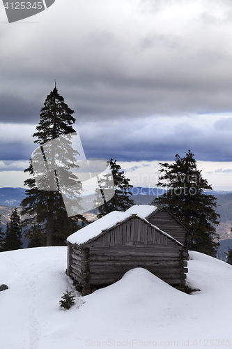 Image of Old wooden hut in winter snow mountains and gray sky with clouds