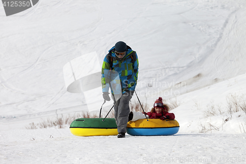 Image of Father and daughter with snow tube in sun winter day