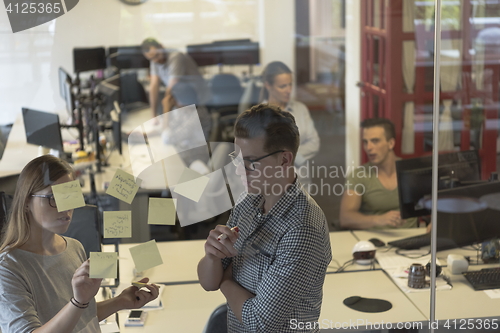 Image of young couple at modern office interior writing notes on stickers