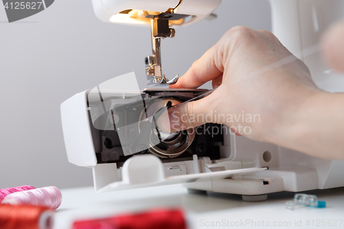 Image of Arm inserts bobbin in sewing-machine