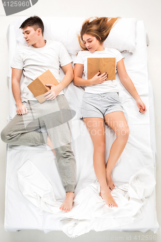 Image of The young lovely couple lying in a bed with books