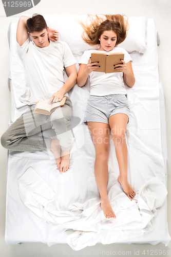 Image of The young lovely couple lying in a bed with books