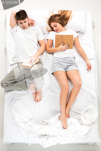 Image of The young lovely couple lying in a bed with books