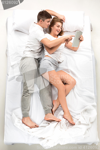 Image of The young lovely couple lying in a bed with laptop