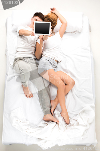 Image of The young lovely couple lying in a bed with laptop