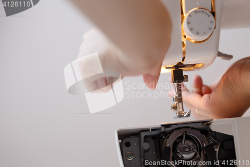 Image of Woman inserts thread in sewing-machine