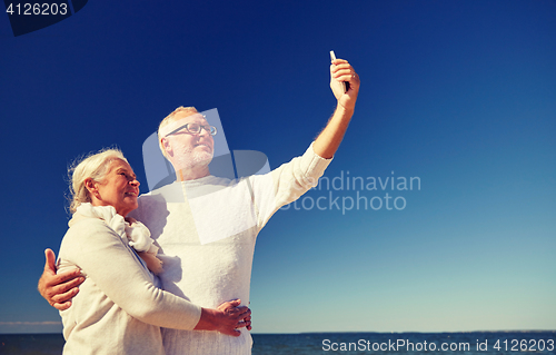 Image of seniors with smartphone taking selfie on beach