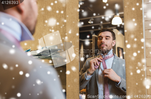 Image of man tying tie on at mirror in clothing store