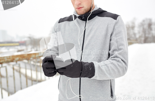 Image of man in earphones with smartphone on winter bridge
