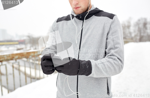 Image of man in earphones with smartphone on winter bridge