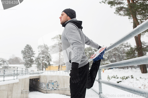 Image of sports man stretching leg at fence in winter