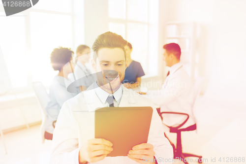 Image of happy doctor with tablet pc over team at clinic