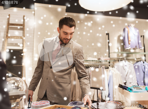 Image of happy young man choosing shirt in clothing store