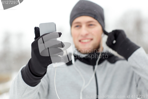 Image of happy man with earphones and smartphone in winter