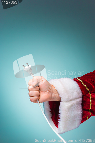 Image of Hand of Santa Claus holding a electrical plug on blue background